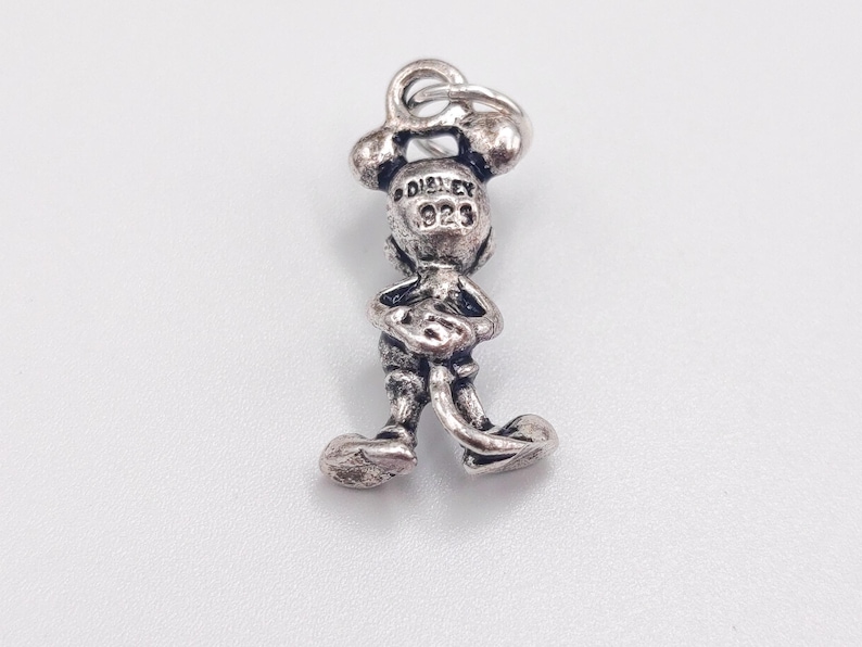Pode incluir: Um berloque de metal em tom prateado com o formato de uma figura de rato de desenho animado em p&eacute;. A parte de tr&aacute;s da cabe&ccedil;a apresenta o texto em relevo DISNEY e 925. O berloque inclui um pequeno anel circular no topo para fixa&ccedil;&atilde;o.
