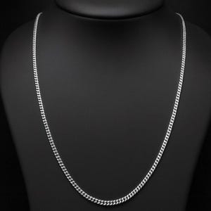 Può includere: Una collana a catena a maglia curb color argento esposta su un manichino nero. La catena è composta da piccole maglie ad incastro, creando un design liscio e continuo. La collana è un classico gioiello.