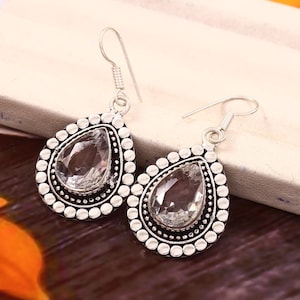 May include: A pair of silver drop earrings. Each earring has a clear, teardrop-shaped gemstone with a beaded border. The earrings have a hook closure.