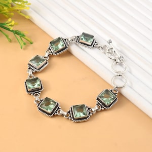 May include: A silver link bracelet featuring six square-cut, light green translucent gemstones. Each stone is set in a decorative, twisted silver frame. The bracelet is secured with a silver toggle clasp consisting of a circular ring and a T-bar.