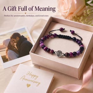 May include: A gift set featuring a purple beaded bracelet with a silver clasp, presented in a pink gift box. The image includes a photo of a couple and a card that says "Happy Anniversary". The text at the top says "A Gift Full of Meaning".
