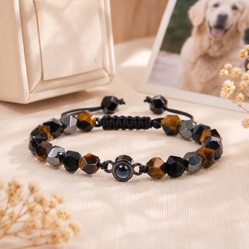 May include: A beaded bracelet featuring faceted black, brown, and gray stones. The bracelet has a black adjustable cord and a small, dark-colored central bead. The stones are arranged in a repeating pattern.