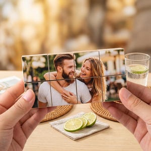 Peut inclure: Un cube photo en bois présentant un couple souriant, tenu dans les mains. Le cube est composé de neuf blocs individuels, chacun affichant une partie de l'image. L'arrière-plan comprend un verre d'eau avec une tranche de citron vert et des tranches de citron vert sur une serviette.