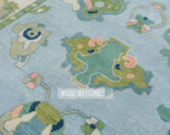 May include: A light blue area rug featuring a repeating pattern of abstract shapes in shades of green, cream, and soft pink. The rug includes a border with a geometric design and the text RUG RITUALS printed in white in the center of the field.