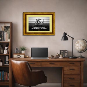 May include: Framed artwork with a gold and brown border. The image features a black and white illustration of a fish riding a bicycle. The text reads: "A woman needs a man like a fish needs a bicycle."