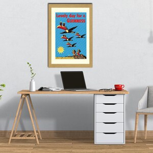 May include: Framed vintage Guinness advertisement featuring toucans in flight, with the text "Lovely day for a Guinness." The artwork is set against a blue sky with a yellow sun and is displayed on a wooden desk.