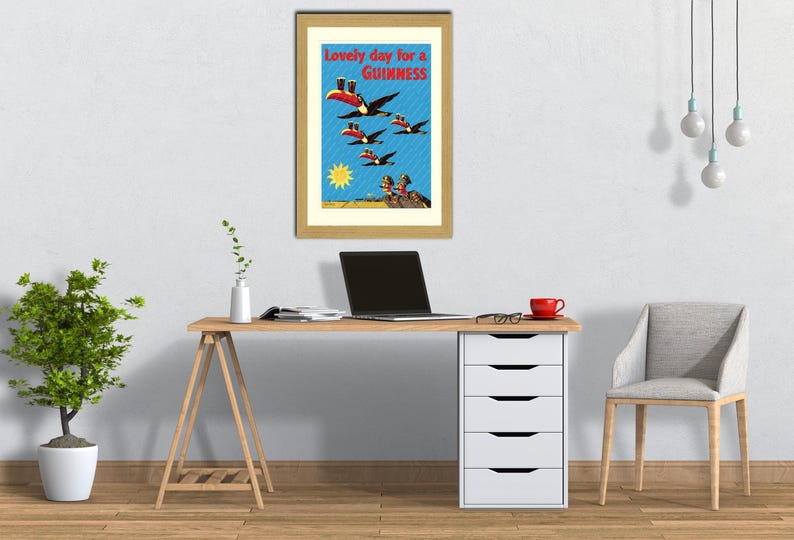May include: Framed vintage Guinness advertisement featuring toucans in flight, with the text "Lovely day for a Guinness." The artwork is set against a blue sky with a yellow sun and is displayed on a wooden desk.