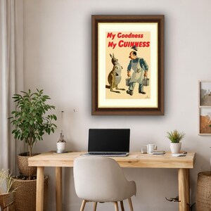 K&ouml;nnte beinhalten: Gerahmte Vintage-Guinness-Werbung mit einem K&auml;nguru und einem Mann mit Eimern. Der Text "My Goodness My Guinness" ist rot dargestellt. Das Kunstwerk befindet sich in einem braunen Rahmen und wird an einer hellen Wand &uuml;ber einem Holzschreibtisch gezeigt.