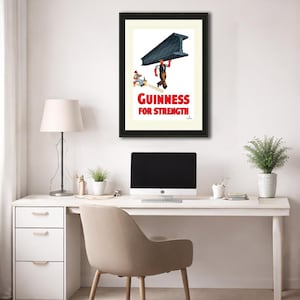 May include: Framed vintage Guinness advertisement. The print features a worker carrying a large steel beam, with the text "Guinness For Strength" in red. The artwork is set against a white background, framed in black.