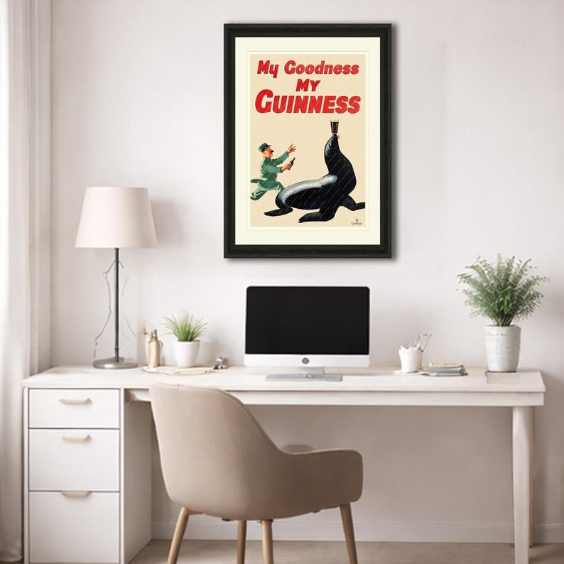 May include: Framed vintage Guinness advertisement featuring a black seal balancing a pint of Guinness. The poster has the text "My Goodness My Guinness" in red and black. A man in a green uniform is running towards the seal.