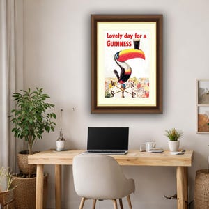 Puede incluir: Anuncio vintage enmarcado de Guinness con un tuc&aacute;n sosteniendo una pinta de Guinness. La obra de arte incluye el texto "Lovely day for a Guinness" en letras rojas. El tuc&aacute;n tiene un pico grande rojo y amarillo.