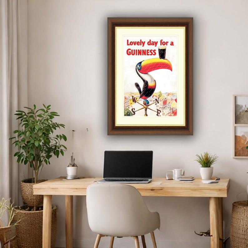 Puede incluir: Anuncio vintage enmarcado de Guinness con un tuc&aacute;n sosteniendo una pinta de Guinness. La obra de arte incluye el texto "Lovely day for a Guinness" en letras rojas. El tuc&aacute;n tiene un pico grande rojo y amarillo.