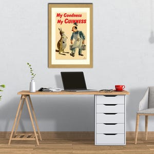K&ouml;nnte beinhalten: Ein gerahmtes Vintage-Guinness-Poster mit einem K&auml;nguru und einem Mann in einer Arbeitssch&uuml;rze. Der Text "My Goodness My Guinness" ist in Rot und Schwarz dargestellt. Das Poster befindet sich auf einem Schreibtisch mit einem Laptop, einer roten Tasse und einem Stuhl.