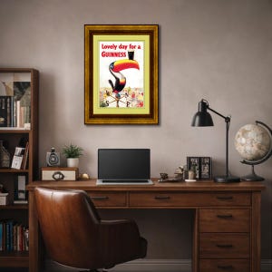 Puede incluir: Anuncio vintage enmarcado de Guinness con un tuc&aacute;n con un pico grande y colorido, sosteniendo una pinta de Guinness. El texto dice "Lovely day for a Guinness". La obra de arte est&aacute; en un marco dorado.