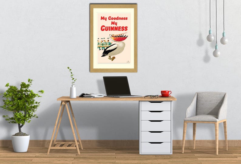 May include: A framed vintage advertisement for Guinness stout. The artwork features a pelican carrying a tray of drinks, with the text "My Goodness My Guinness" in red and white. The frame is a light wood color.