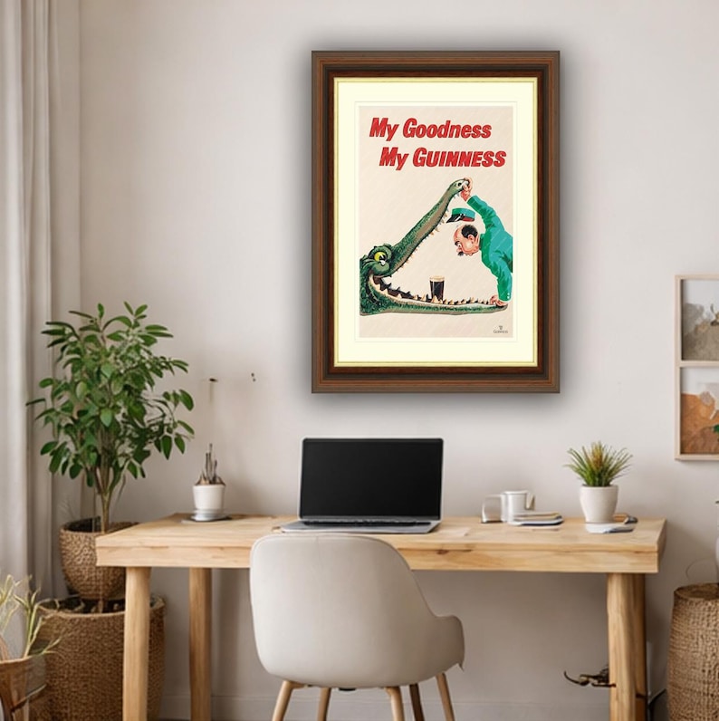 May include: Framed vintage Guinness advertisement. The artwork shows a man in a green suit pouring a pint of Guinness into a crocodile's mouth. The text reads "My Goodness My Guinness." The frame is brown.