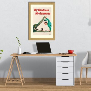 May include: Framed vintage Guinness advert showing a cartoon of a man in a green suit pouring a pint of Guinness into an alligator's mouth. The text reads "My Goodness My Guinness" in red.