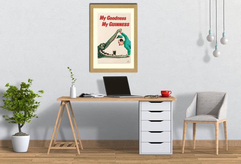 May include: Framed vintage Guinness advert showing a cartoon of a man in a green suit pouring a pint of Guinness into an alligator's mouth. The text reads "My Goodness My Guinness" in red.