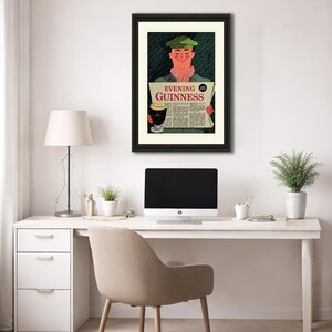 May include: Framed vintage advertisement for Guinness stout. The artwork features a smiling man in a green cap holding a newspaper with the headline "Evening Guinness." A pint of Guinness is also depicted. The frame is black, and the artwork is displayed on a white wall.