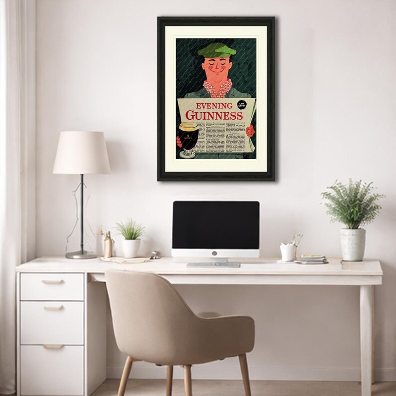 May include: Framed vintage advertisement for Guinness stout. The artwork features a smiling man in a green cap holding a newspaper with the headline "Evening Guinness." A pint of Guinness is also depicted. The frame is black, and the artwork is displayed on a white wall.