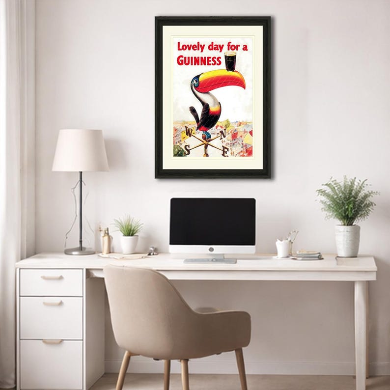 Puede incluir: Anuncio vintage enmarcado de Guinness con un tuc&aacute;n sosteniendo una pinta de Guinness. El tuc&aacute;n tiene un pico grande rojo y amarillo. El texto en la parte superior dice "Lovely day for a Guinness". La obra de arte est&aacute; sobre un fondo crema.