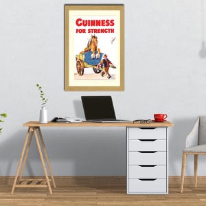 K&ouml;nnte beinhalten: Gerahmte Vintage-Guinness-Werbung. Der Druck zeigt einen Pferdewagen mit einem Mann und dem Text "Guinness for Strength" in Rot und Wei&szlig;. Der Rahmen hat eine hellbraune Farbe.