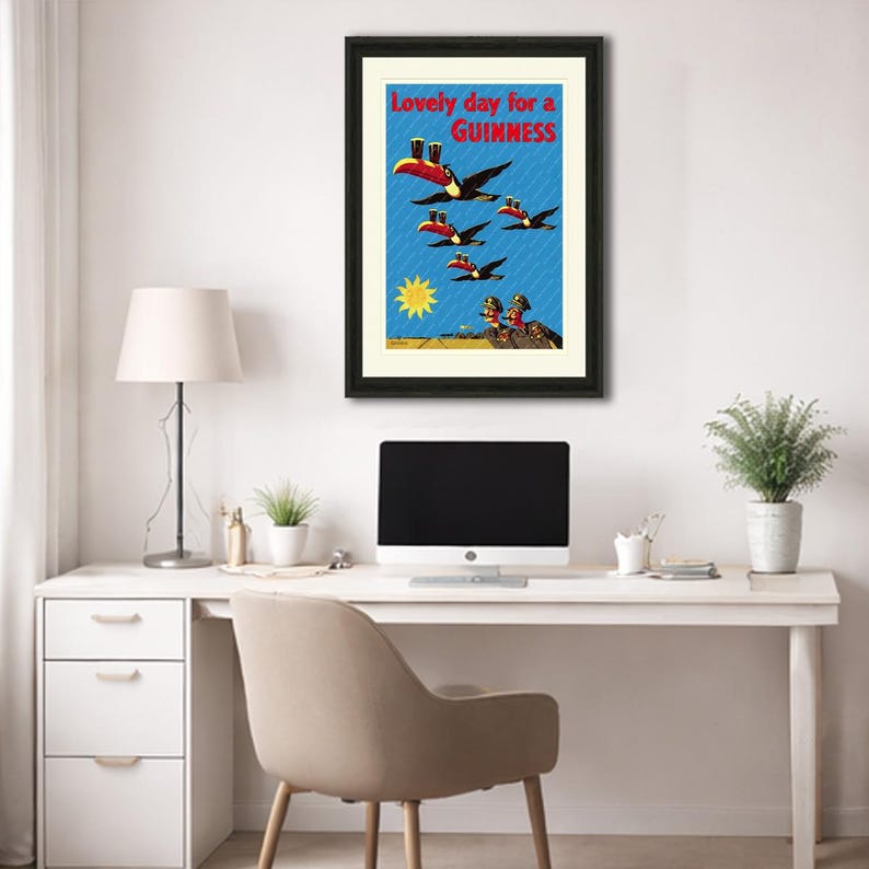 May include: Framed vintage Guinness advertisement featuring toucans carrying pints of Guinness against a blue background with the text "Lovely day for a Guinness." The artwork includes a yellow sun and figures at the bottom.