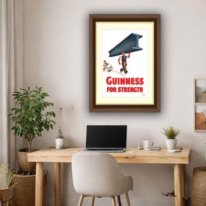 May include: Framed vintage Guinness advertisement. The print features a worker carrying a large steel beam, with the text "Guinness For Strength" in red. The artwork is set against a white background with a cream-colored matting, and a dark brown frame.