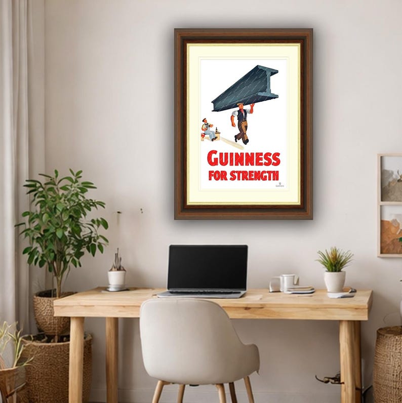 May include: Framed vintage Guinness advertisement. The print features a worker carrying a large steel beam, with the text "Guinness For Strength" in red. The artwork is set against a white background with a cream-colored matting, and a dark brown frame.