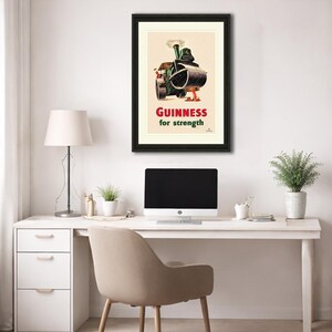 Puede incluir: Anuncio vintage enmarcado de Guinness. La obra de arte presenta un rodillo de vapor con un barril de Guinness, con el texto "Guinness for strength" en rojo y blanco. El p&oacute;ster est&aacute; en un marco negro.