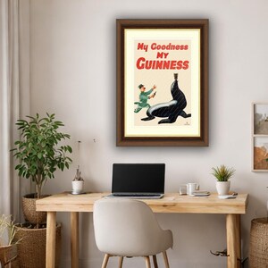 May include: Framed vintage Guinness advertisement featuring a black seal balancing a crown, with a man in a green uniform running towards it. The text reads "My Goodness My Guinness" in red and black.