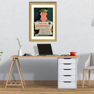 May include: A framed vintage advertisement for Guinness stout. The artwork depicts a man in a green cap reading a newspaper with the headline "Evening Guinness." The image is set in a home office with a desk, chair, and a potted plant.