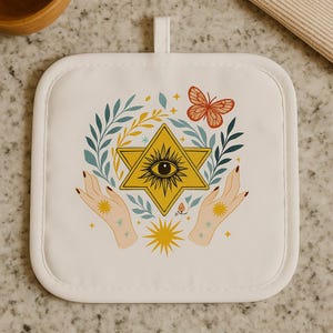 May include: White square pot holder with a hanging loop. The design features a yellow star with an eye, surrounded by leaves, a butterfly, and hands. The pot holder has a white border and is on a light-colored surface.