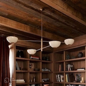 May include: A modern chandelier with five off-white bowl-shaped shades. The fixture has a brass finish and is suspended from the ceiling. The light fixture is in a room with wooden shelves and a wooden ceiling.