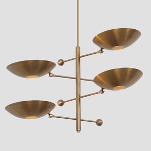 Peut inclure: Un lustre moderne en laiton avec quatre luminaires en forme de bol. Les lumières sont disposées sur des bras horizontaux s'étendant d'une tige verticale centrale. Chaque bol a une source de lumière chaude.