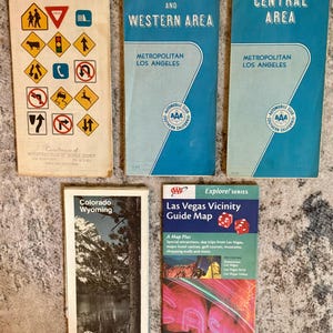 May include: Five vintage paper travel maps including a Rand McNally California map with road signs, two blue Automobile Club of Southern California maps for Central and Western Los Angeles, a Colorado Wyoming map, and a Las Vegas Vicinity Guide Map.