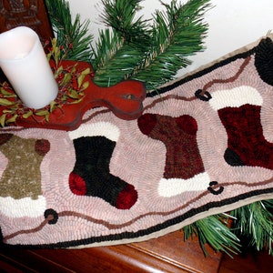 May include: A pink and brown rug with three embroidered stockings in black, red, and white. The stockings are decorated with a white cuff and a brown loop at the top. The rug is decorated with a brown border and a black and white pattern.
