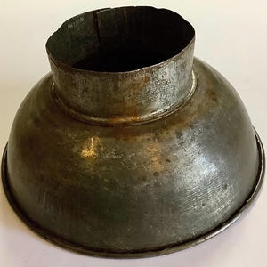 May include: A vintage metal funnel with a wide, rounded base and a narrower, cylindrical top. The funnel has a weathered, aged appearance with visible rust and discoloration, suggesting it is an antique or has been well-used.