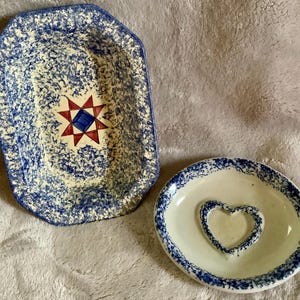 May include: Two ceramic dishes. One is a rectangular serving dish with a blue and white speckled pattern and a red and blue star design. The other is a small, round dish with a heart-shaped indentation and a blue speckled rim.