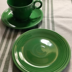 May include: A set of green ceramic dishes, including a teacup, saucer, and a larger plate. The dishes have a glossy finish and a simple, elegant design.