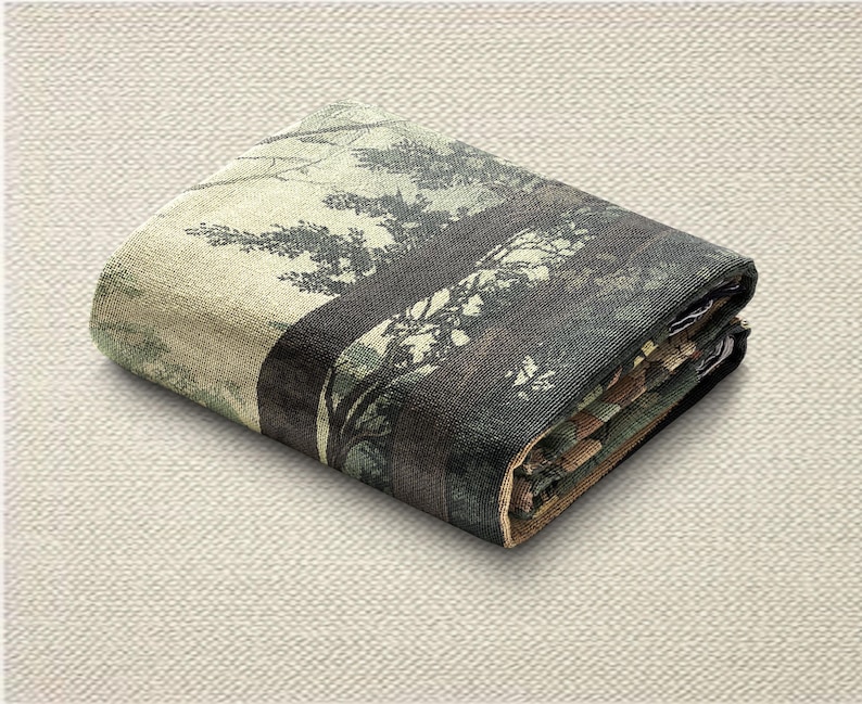 May include: Folded blanket featuring a forest scene with trees in shades of green, brown, and black. The blanket is folded neatly, showcasing the detailed print of the forest landscape. The edges are finished with a contrasting border.