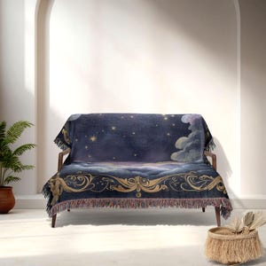 May include: A dark blue throw blanket draped over a wooden sofa. The blanket features a celestial design with stars, clouds, and gold decorative elements. The edges have a fringe trim, adding texture and detail to the cozy home decor item.