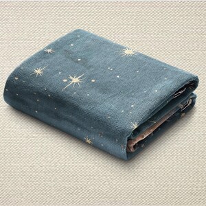 May include: Folded blue fabric featuring a celestial pattern of white stars and sunbursts. The fabric is neatly folded, displaying the design. The background is a neutral, textured surface.