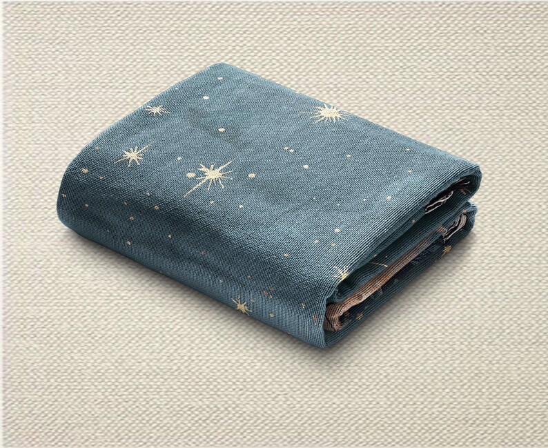May include: Folded blue fabric featuring a celestial pattern of white stars and sunbursts. The fabric is neatly folded, displaying the design. The background is a neutral, textured surface.