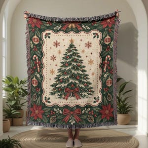 Könnte beinhalten: Eine gewebte Wohndecke mit einem zentralen Weihnachtsbaum-Motiv auf cremefarbenem Grund, umrahmt von einem dunkelgrünen Rand mit Weihnachtssternen, Tannenzapfen, Zuckerstangen und Christbaumkugeln. Die Decke hat Fransen an der Ober- und Unterseite.