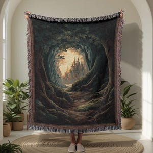 Può includere: Una coperta arazzo tessuta raffigurante un paesaggio fantasy con un sentiero che conduce a un castello. L'opera d'arte raffigura una foresta con grandi alberi e un castello in lontananza. La coperta ha un bordo con frange.