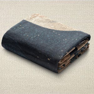 May include: Folded textile with a navy blue and tan color scheme. The navy blue section has a speckled pattern with small tan dots. The tan section has a detailed, patterned design. The textile is folded neatly.