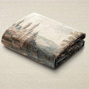 May include: Folded tapestry featuring a detailed castle scene with towers, bridges, and surrounding landscape in shades of brown, blue, and beige. The fabric is folded neatly, showcasing the intricate design and texture.