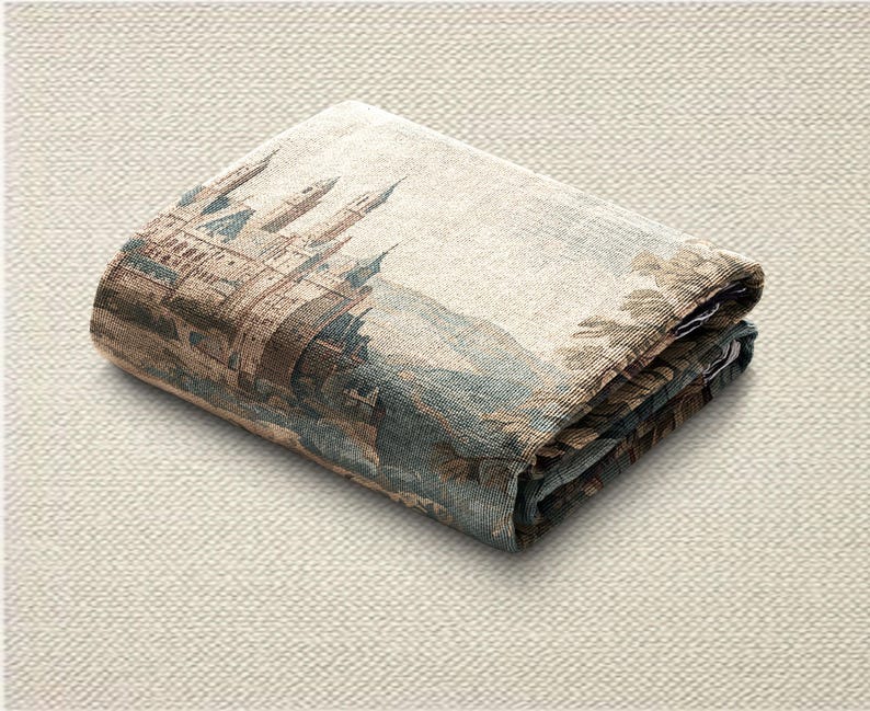 May include: Folded tapestry featuring a detailed castle scene with towers, bridges, and surrounding landscape in shades of brown, blue, and beige. The fabric is folded neatly, showcasing the intricate design and texture.