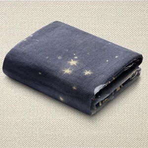 May include: Folded navy blue fabric with a constellation pattern featuring gold stars and white dots. The fabric is folded neatly, showcasing the design on the top layer. The fabric is likely a textile, possibly for crafting or home decor.